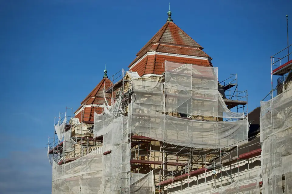 Bâtiment de brique aux toits pointus, échafaudé et bâché pendant des travaux